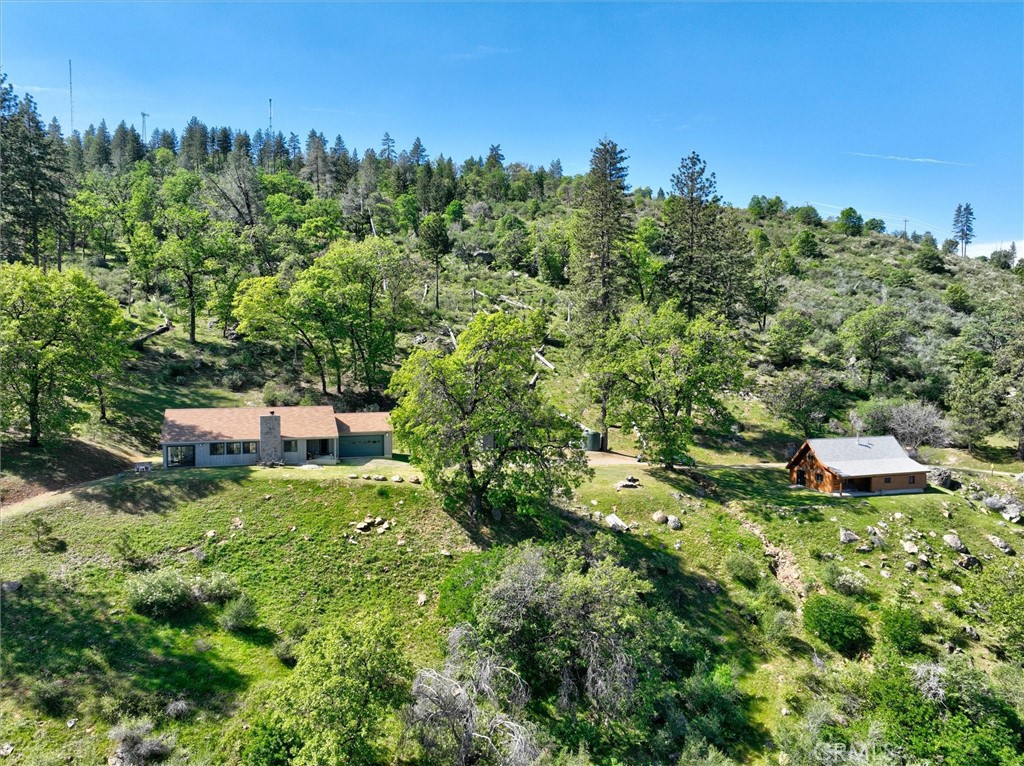 Two homes sit apart on a wooded, rocky hillside beneath a clear blue sky.