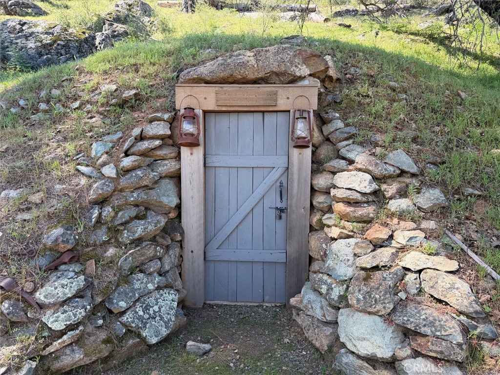Wooden door set into a rocky hillside, flanked by stacked stone walls and two lanterns.