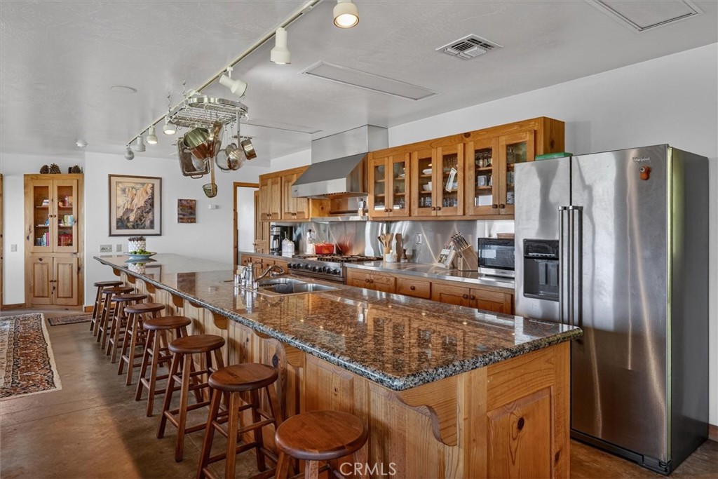 Kitchen with a long granite island, wooden bar stools, wood cabinetry, and stainless steel appliances.