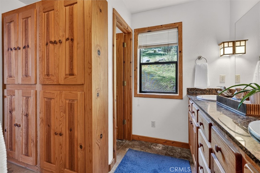 Bathroom with honey-toned wood cabinetry, granite countertop, and a window overlooking a grassy hillside.