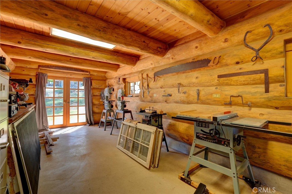 Woodworking workshop with log walls, large machinery, and glass-paneled double doors.