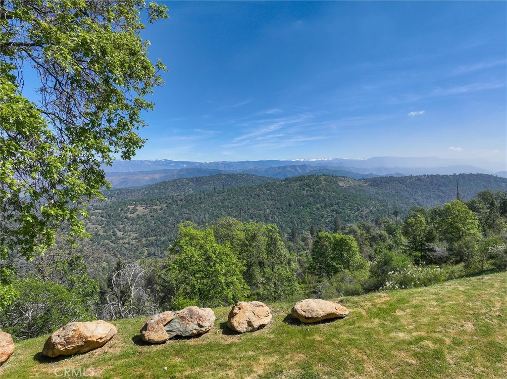 Panoramic mountain view over wooded ridges, framed by foreground rocks and a grassy hillside.