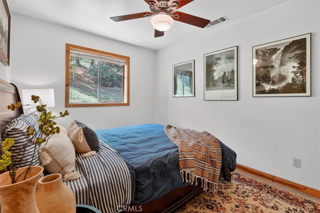 Bedroom with blue bedding, framed landscape photographs, and a window overlooking a wooded hillside.