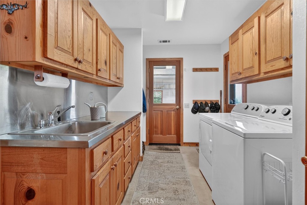 Laundry room with wood cabinetry, stainless-steel sink, and white washer and dryer.
