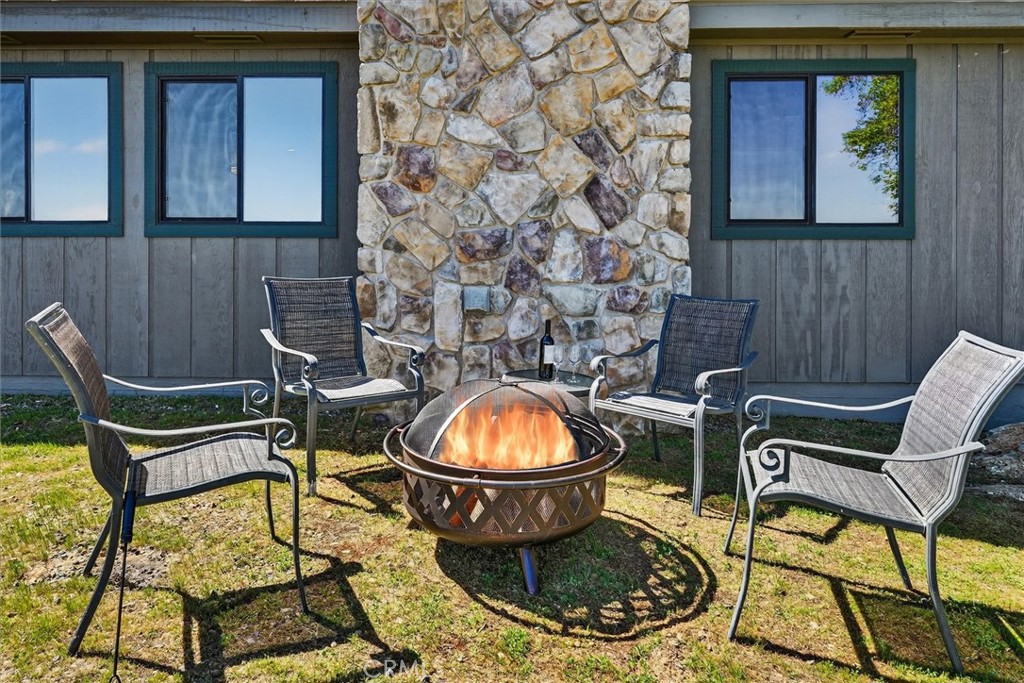 Four patio chairs surround a lit fire pit beside a stone chimney.