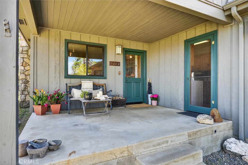 Covered front porch with teal-trimmed doors, a bench, and potted flowers.