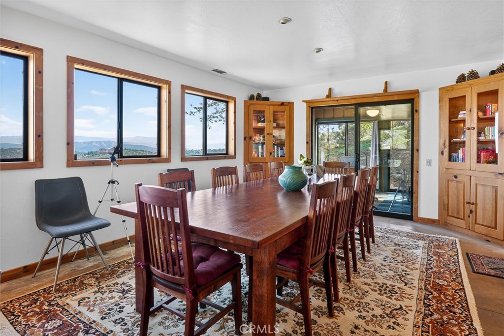 Furnished dining room with a long wooden table, patterned rugs, and mountain views through large windows.