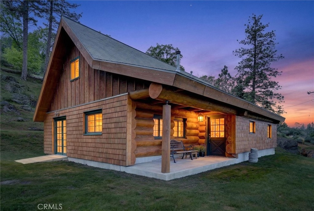 Rustic log cabin at dusk with a covered porch and warmly glowing windows.