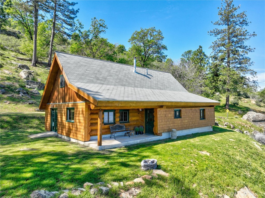 Log cabin with a covered porch on a grassy, pine-covered hillside.
