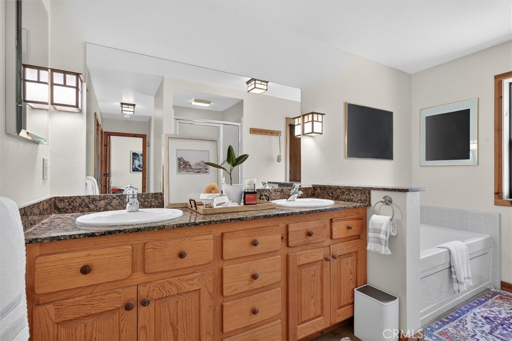 Bathroom with a double-sink granite vanity, warm wood cabinetry, and a bathtub.