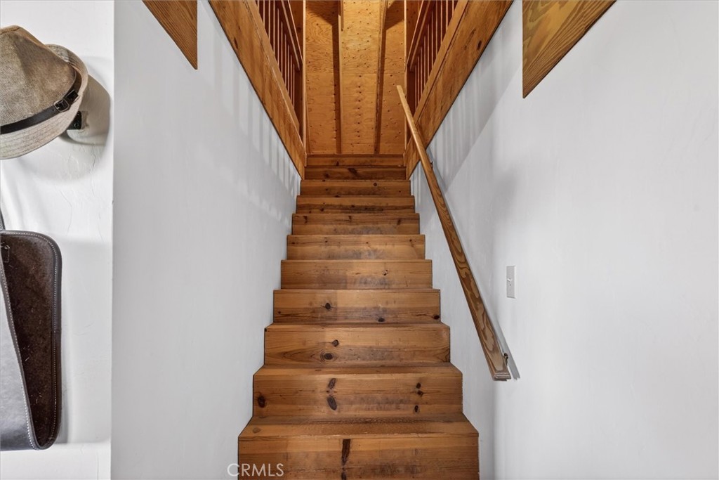 Wooden staircase with broad plank steps, a side handrail, and exposed ceiling beams.