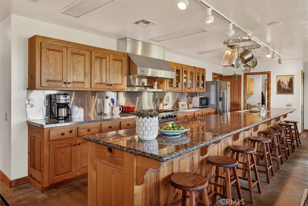 Kitchen with wood cabinets, stainless steel appliances, and a long granite island lined with bar stools.