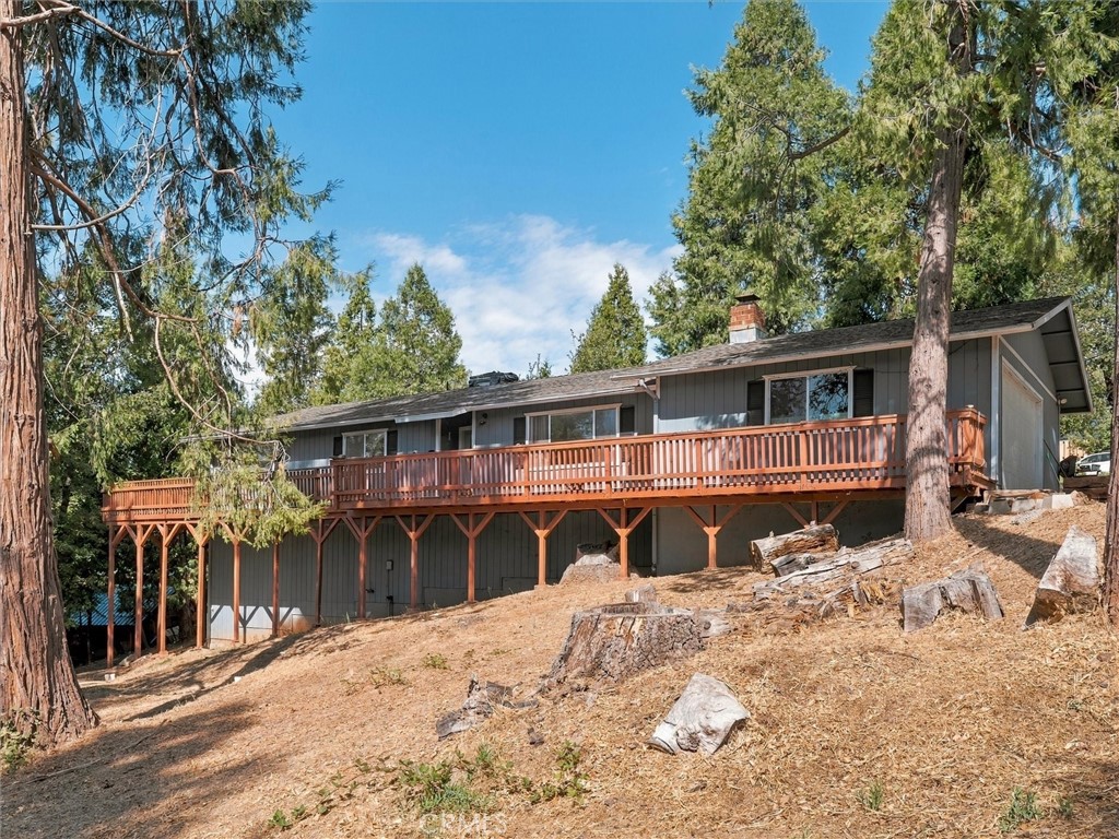 Gray home with a long raised wooden deck on a sloping, tree-lined lot.