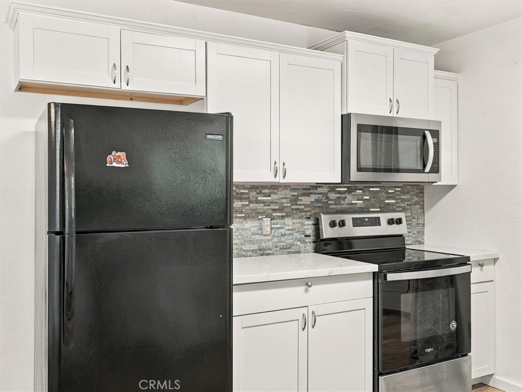 Kitchen with white cabinets, gray mosaic backsplash, black refrigerator, and stainless microwave and range.