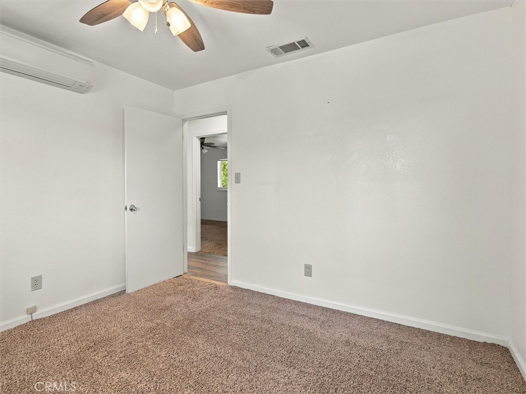 Empty carpeted bedroom with a ceiling fan, wall air conditioner, and open doorway.