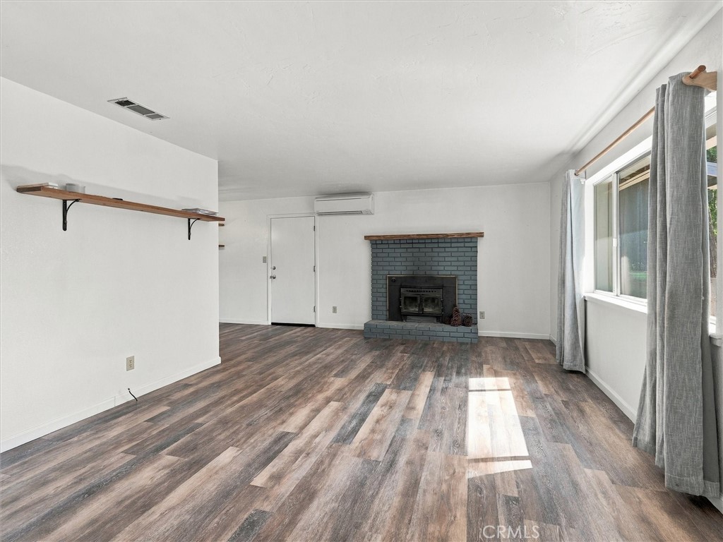 Unfurnished living room with a blue-gray brick fireplace, wood-look flooring, and large curtained windows.