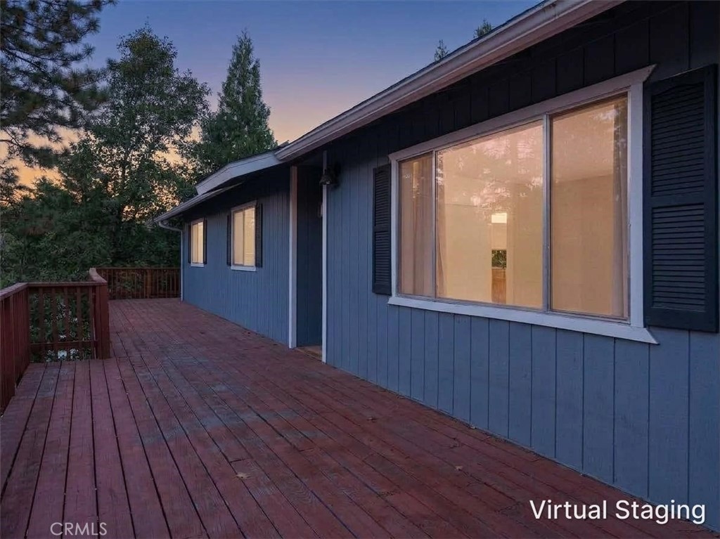 Blue-sided house with a long wooden deck among trees at dusk.
