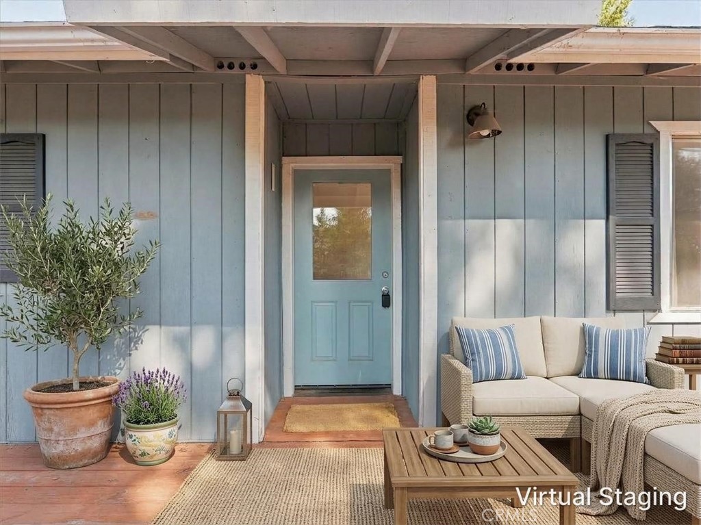 Covered front porch with a pale blue entry door, wicker seating, striped pillows, and potted plants.