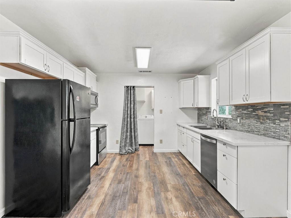 Kitchen with white cabinets, dark appliances, gray tile backsplash, and a washer visible through the back doorway.