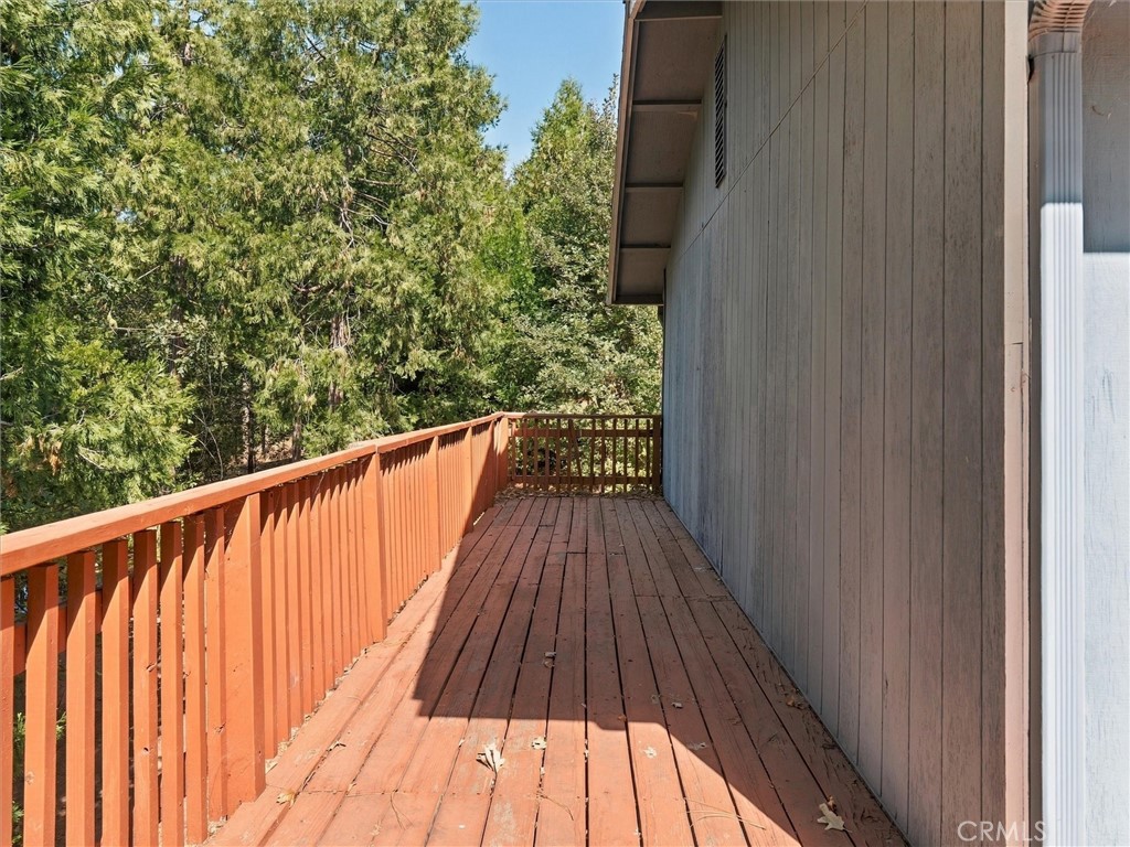 Wooden deck beside a gray-sided house, bordered by red railings and evergreen trees.