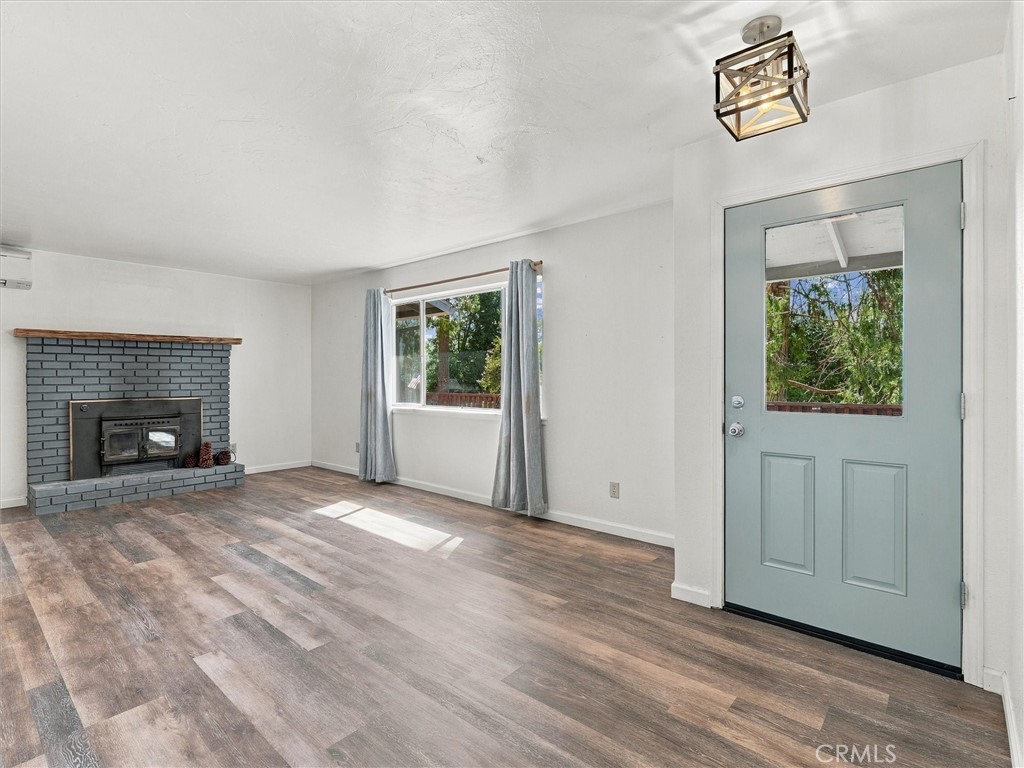 Vacant living room with a gray brick fireplace, wood-look flooring, and pale blue front door.