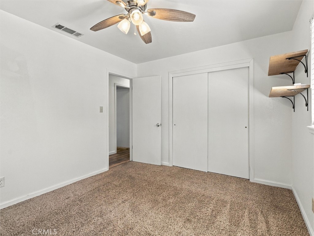 Vacant bedroom with a white sliding-door closet, beige carpet, and ceiling fan.