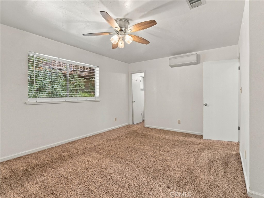 Unfurnished carpeted room with a ceiling fan, window blinds, and wall-mounted air conditioner.