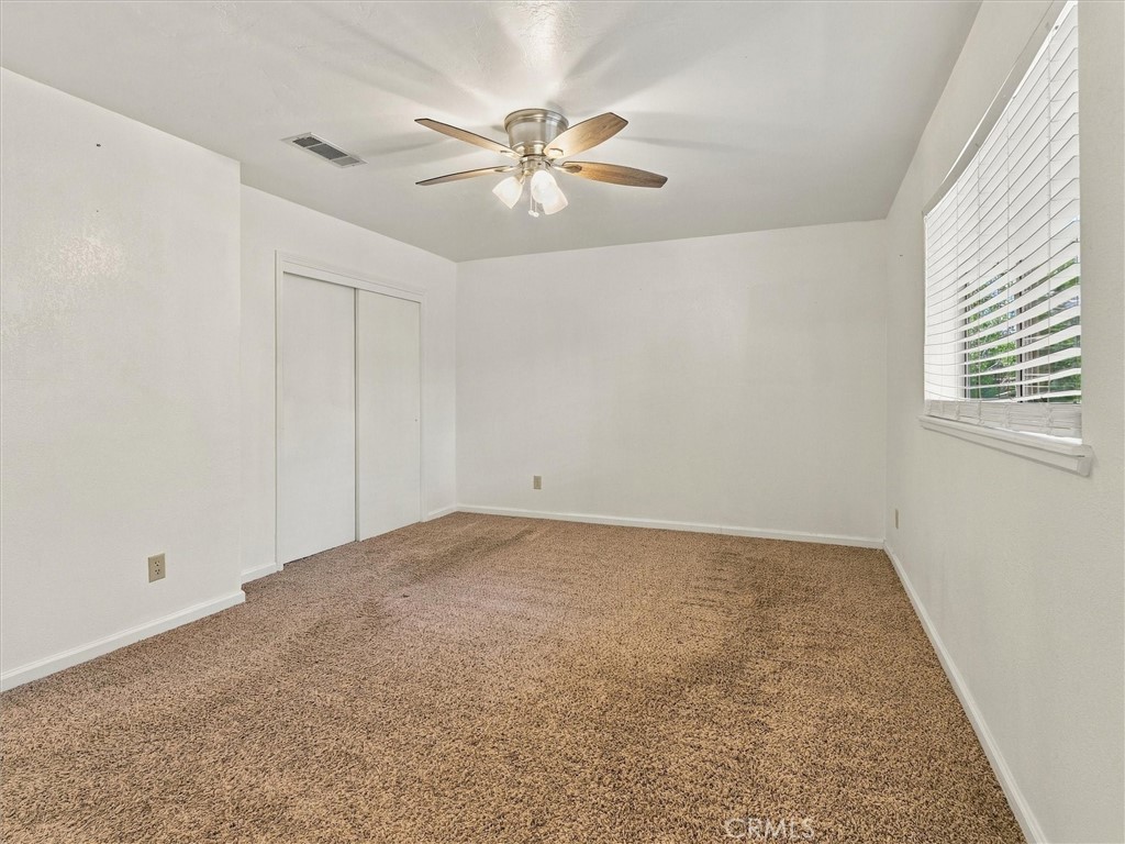 Empty bedroom with tan carpet, sliding closet doors, and a ceiling fan.