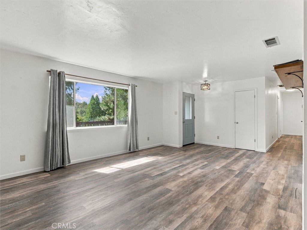 Vacant room with plank flooring and a large curtained window overlooking trees.