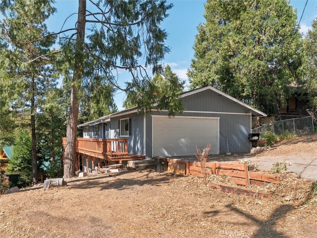 Gray house with a two-car garage and raised wooden deck among tall trees.