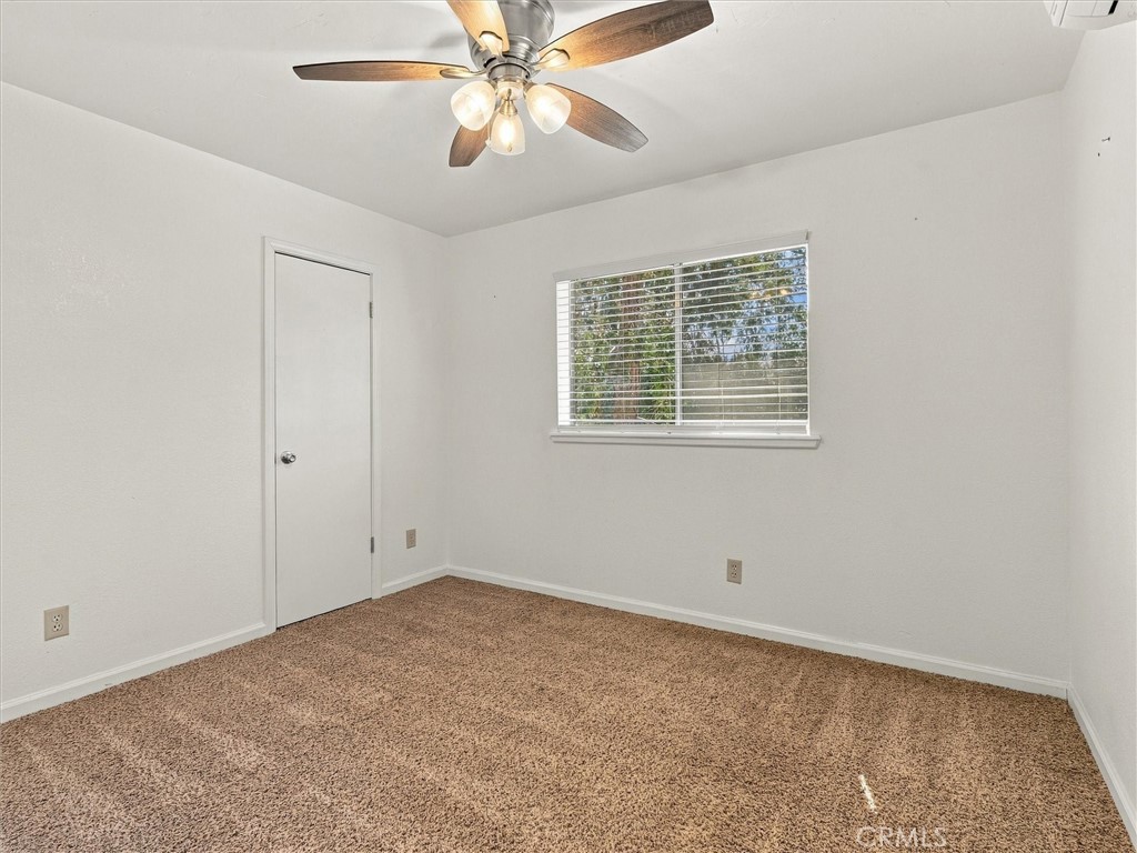 Vacant bedroom with beige carpet, a ceiling fan, and a window with blinds.