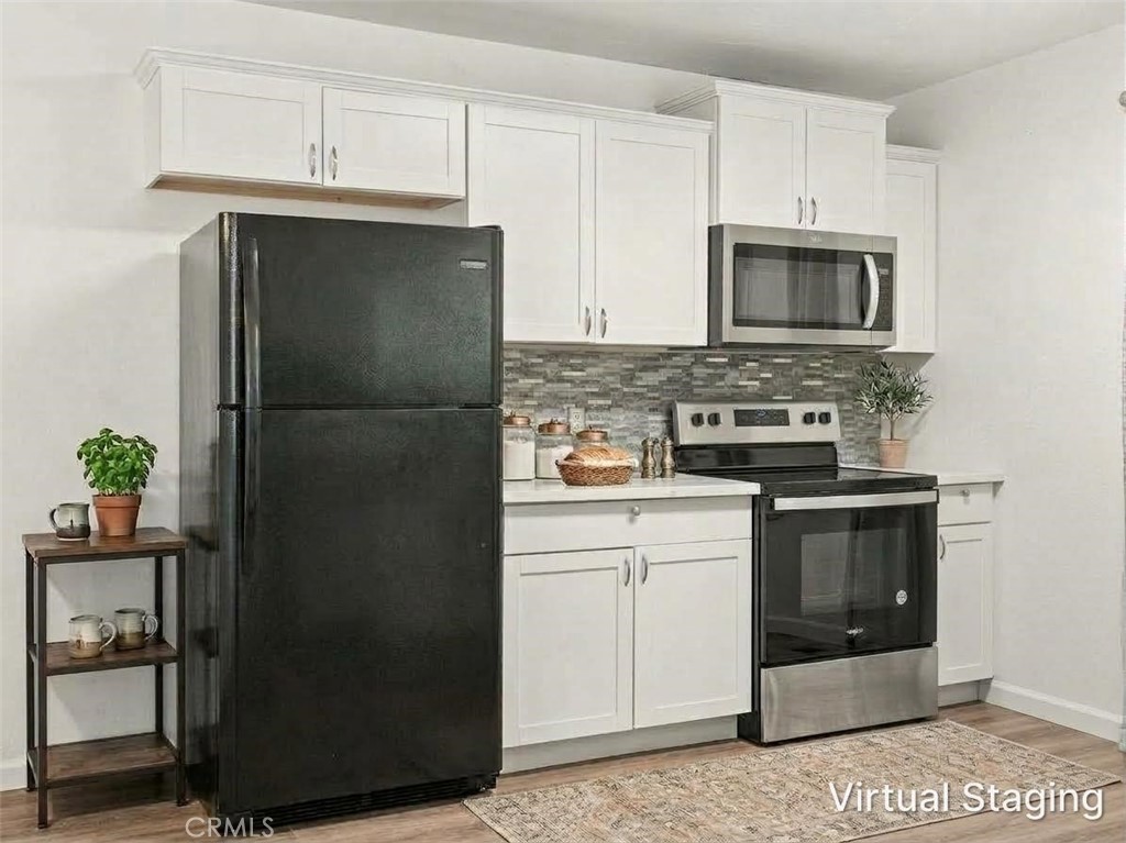 Kitchen with white cabinets, gray tile backsplash, and black appliances, including a refrigerator and range.