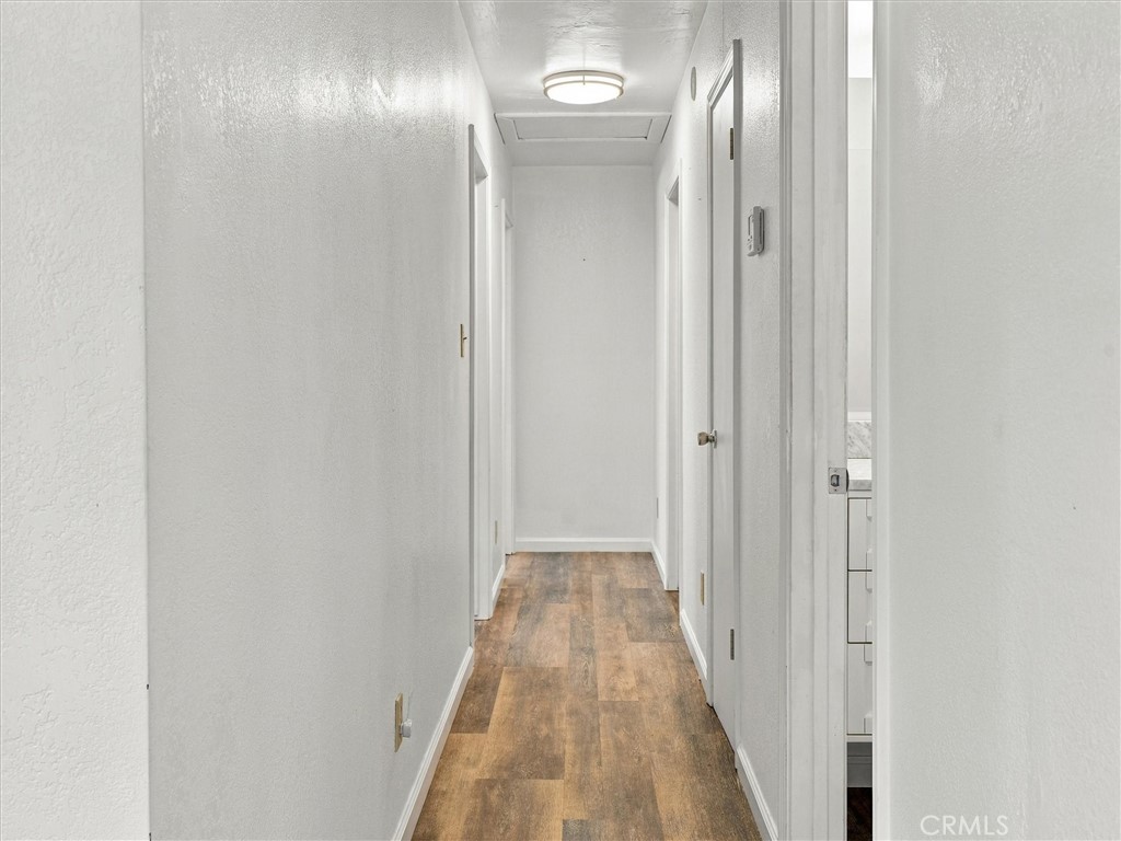 Unfurnished hallway with wood-look flooring, white walls, and several doorways.
