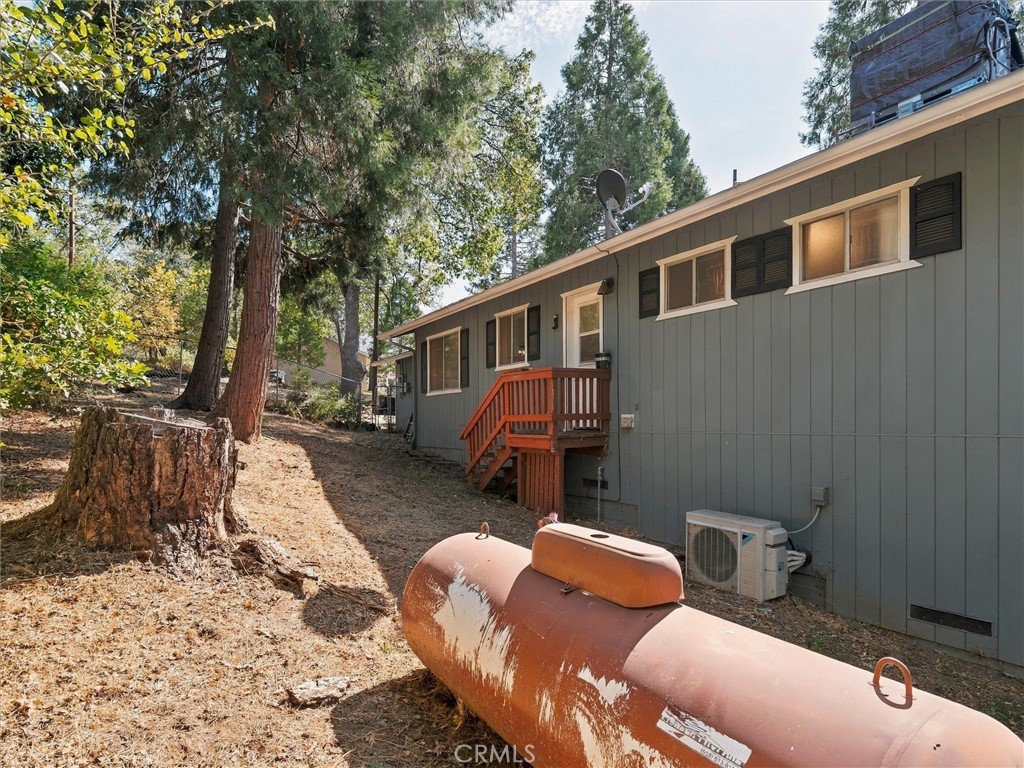 Gray home with wooden entry stairs and a large propane tank on a wooded lot.
