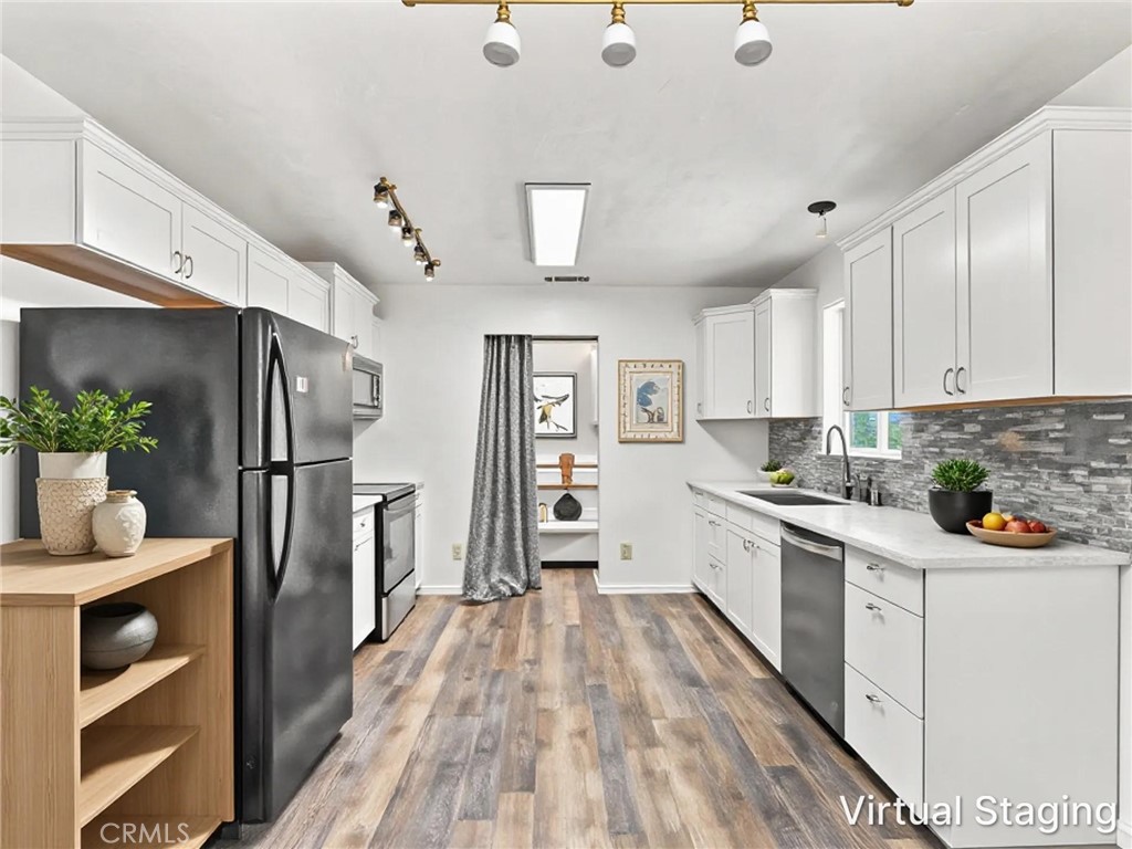 Galley kitchen with white cabinets, gray backsplash, stainless appliances, and wood-look flooring.