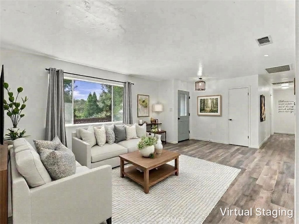Virtually staged living room with white sectional sofas, a wood coffee table, and a large window overlooking trees.
