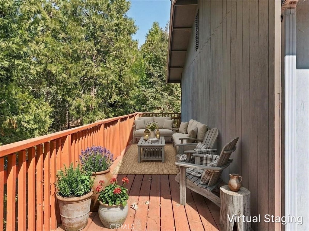 Wooden deck with outdoor seating and potted flowers overlooking trees.