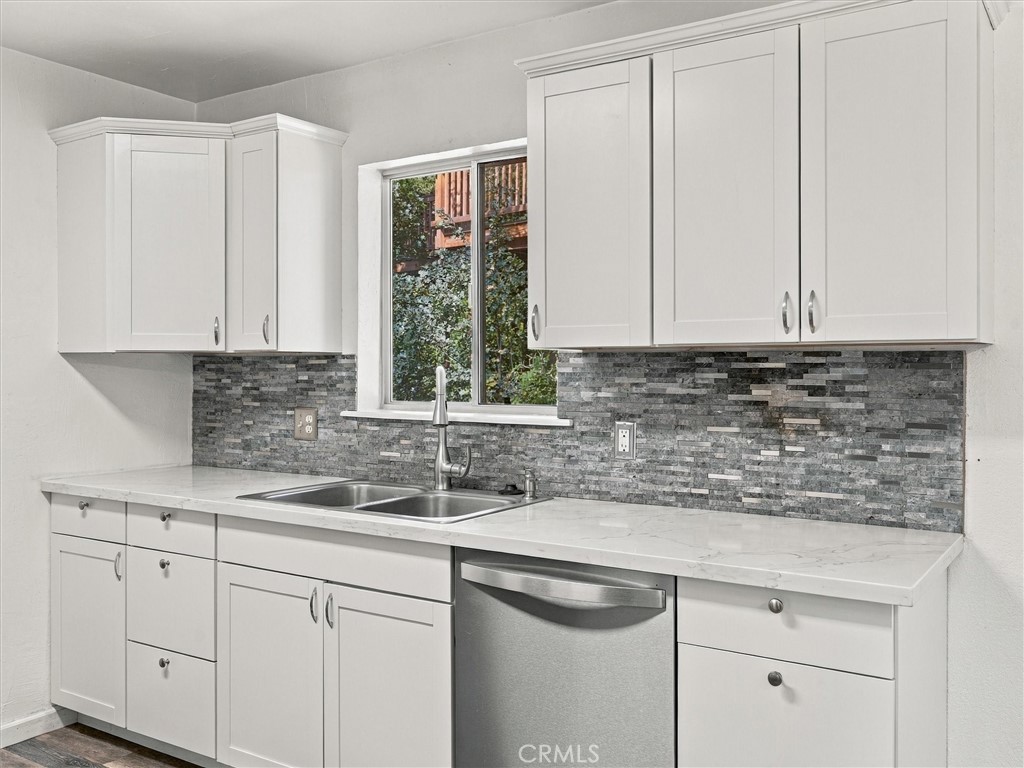 Kitchen with white cabinets, gray mosaic backsplash, double sink, and stainless steel dishwasher.