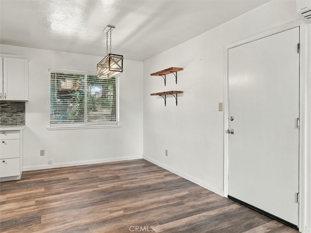 Unfurnished room with wood-look flooring, a front door, window blinds, and floating shelves.
