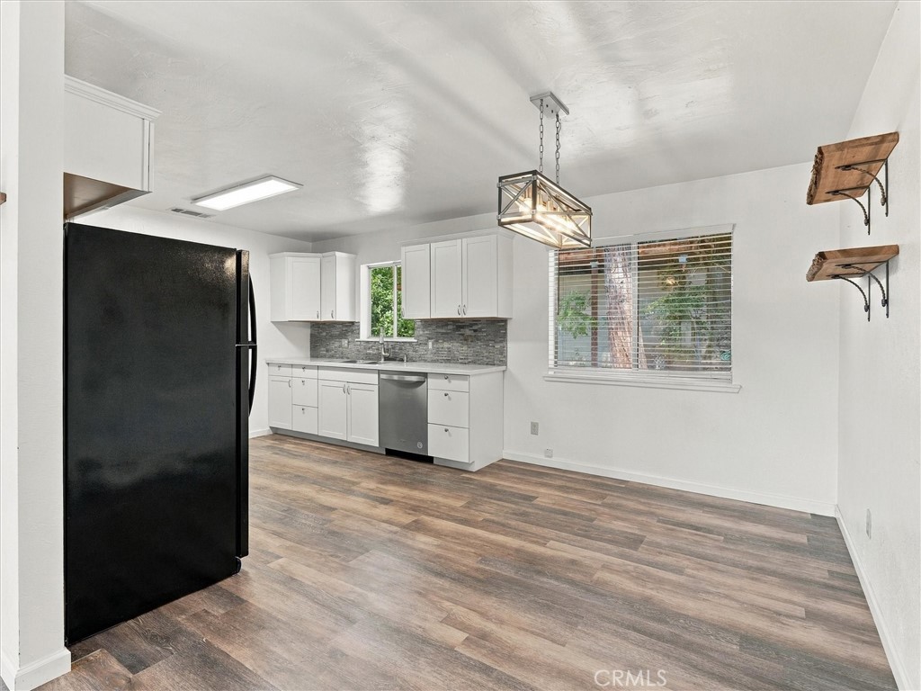 Kitchen with white cabinets, gray tile backsplash, black refrigerator, and wood-look flooring.