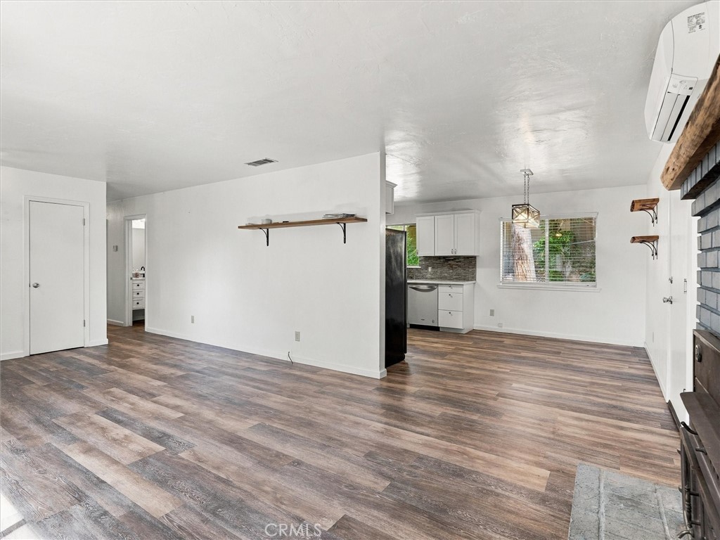 Vacant living area opening to a compact kitchen, with wood-look flooring and a large window.