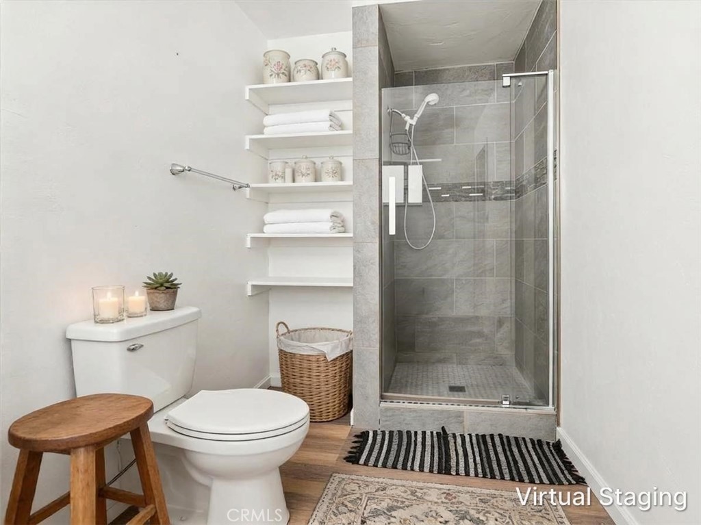 Bathroom with a glass-enclosed gray-tile shower, toilet, and open shelves stocked with towels.
