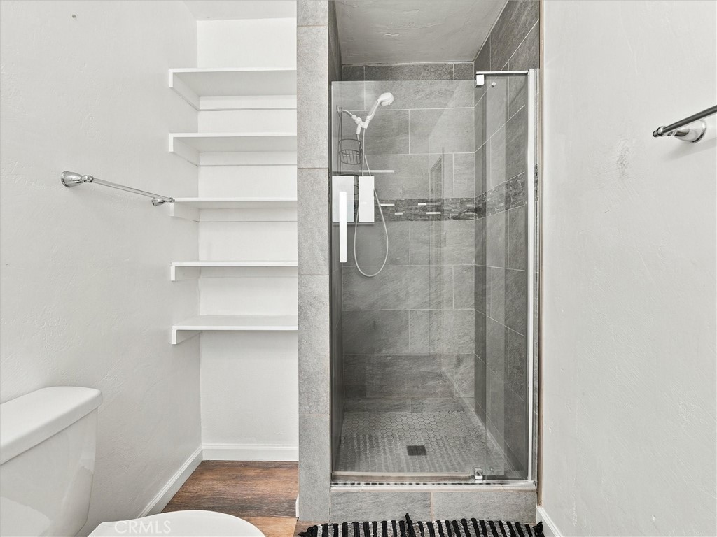 Bathroom with a glass-enclosed gray tiled shower and white built-in shelves.