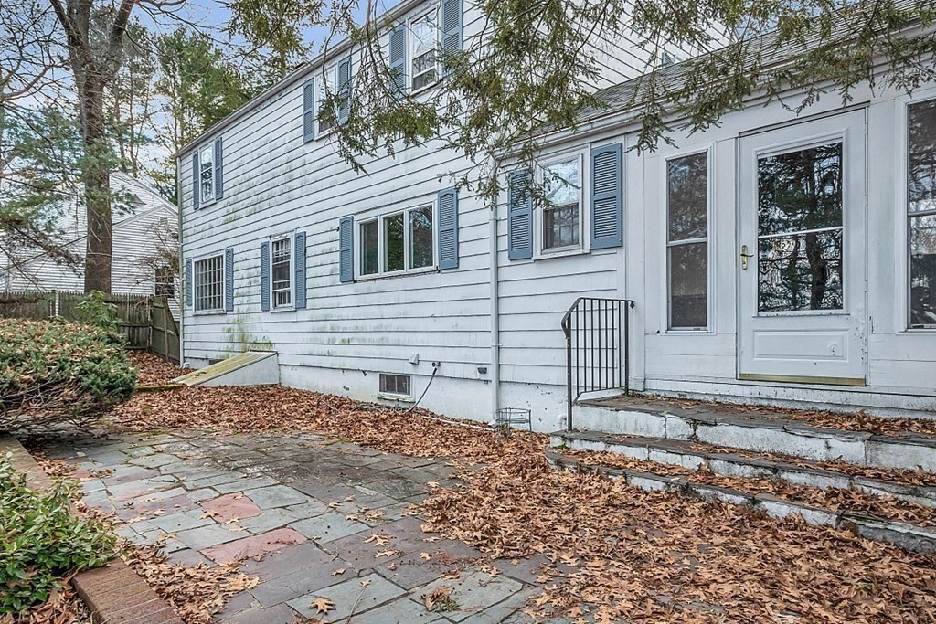 White two-story house with blue shutters and a leaf-strewn stone patio.