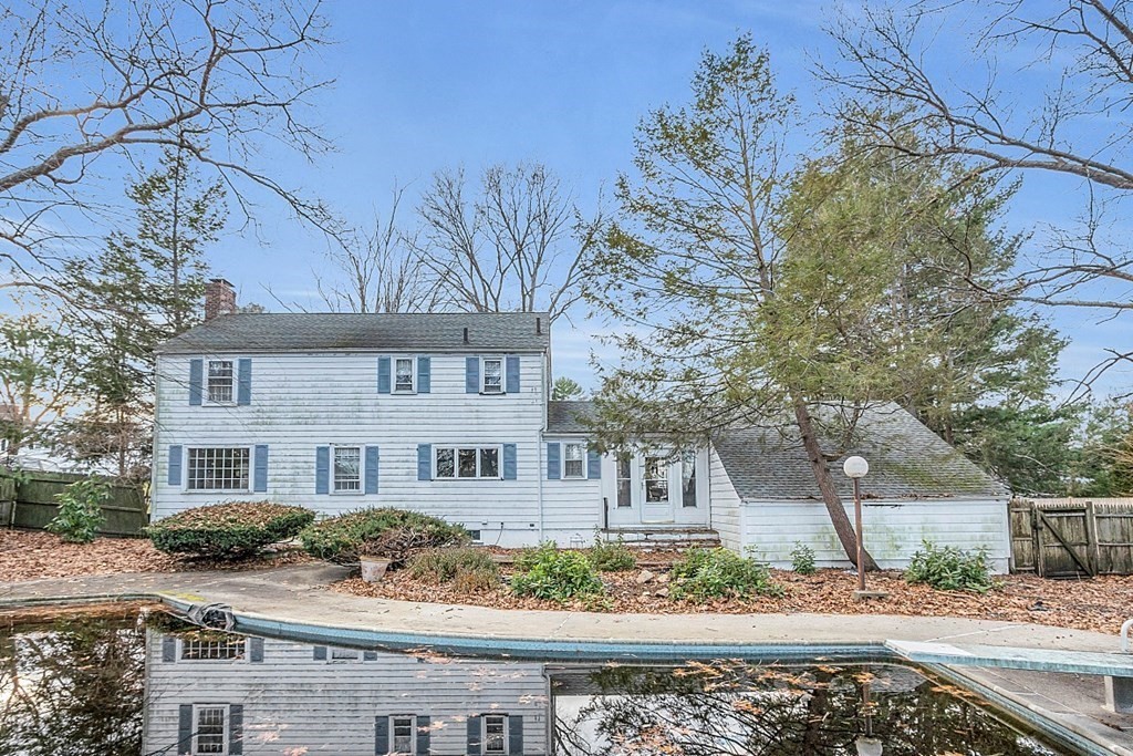 White two-story house with blue shutters behind a swimming pool, framed by bare trees.