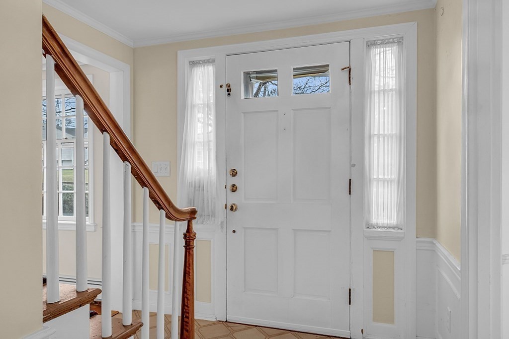 Entry foyer with a white paneled front door and a staircase with a polished wood handrail.