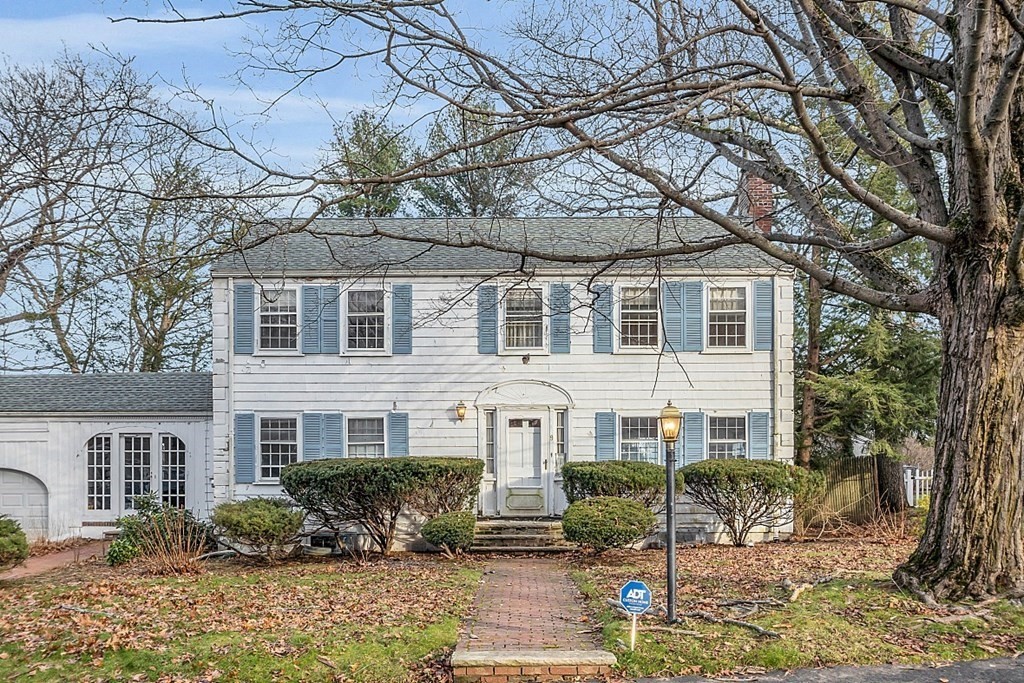 White two-story colonial home with blue shutters, attached garage, and brick front walkway.