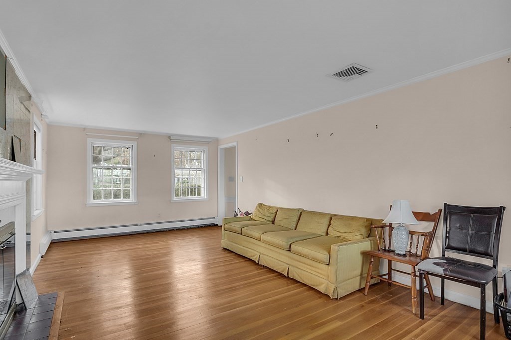 Living room with a yellow sofa, hardwood floors, two windows, and a fireplace.