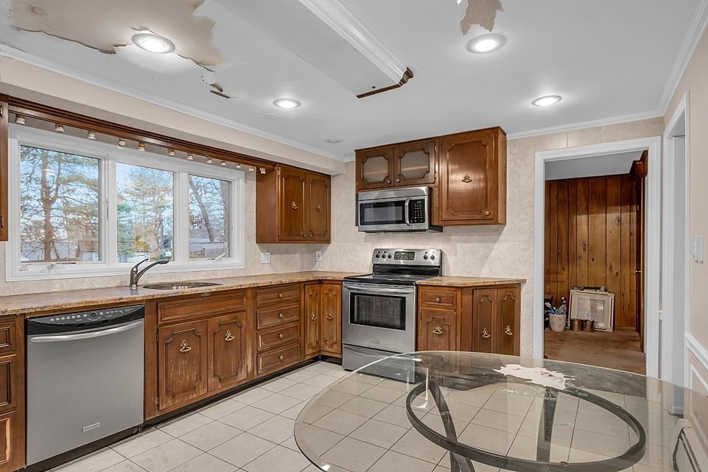 Kitchen with dark wood cabinets, stainless-steel appliances, and peeling ceiling paint.