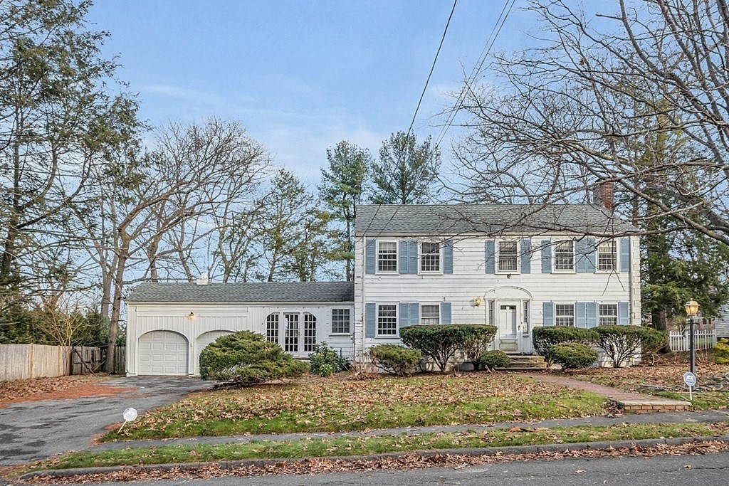 White two-story Colonial with blue shutters, attached garage, and a leaf-covered front lawn.